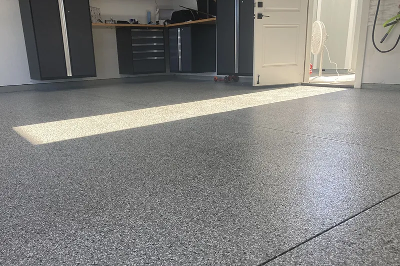 Sunlit garage with gray flake epoxy floor and cabinets
